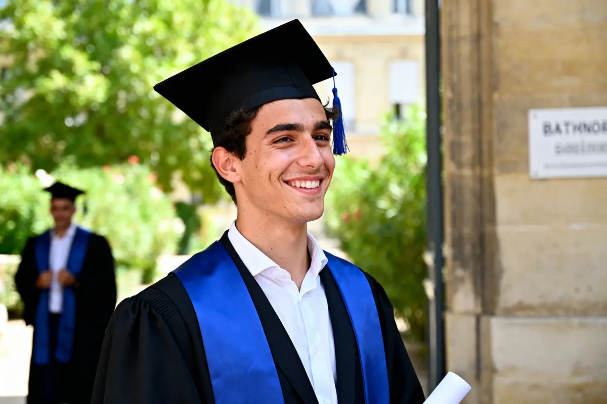 Élève diplômé souriant tenant son diplôme lors d'une cérémonie de bachlor universitaire