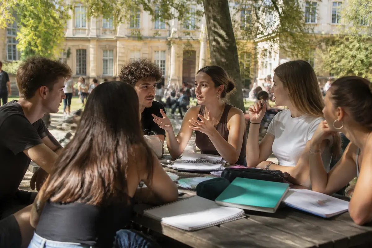 Des étudiants discutent au sein d'une association estudiantine en plein air sur un campus.