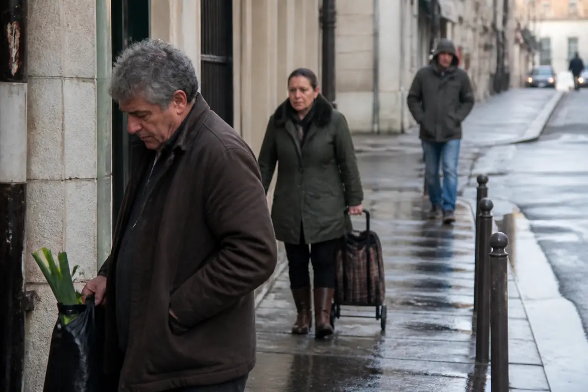 Passants fatalistes sur trottoir urbain mouillé, portant parapluies et cabas